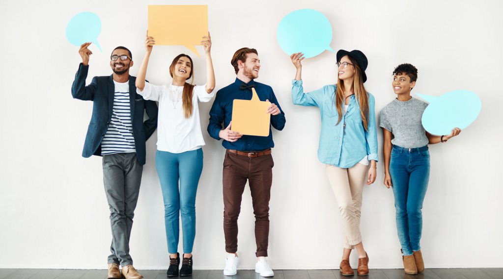 Diverse group of employees holding colorful speech bubbles, standing inside a modern office space.