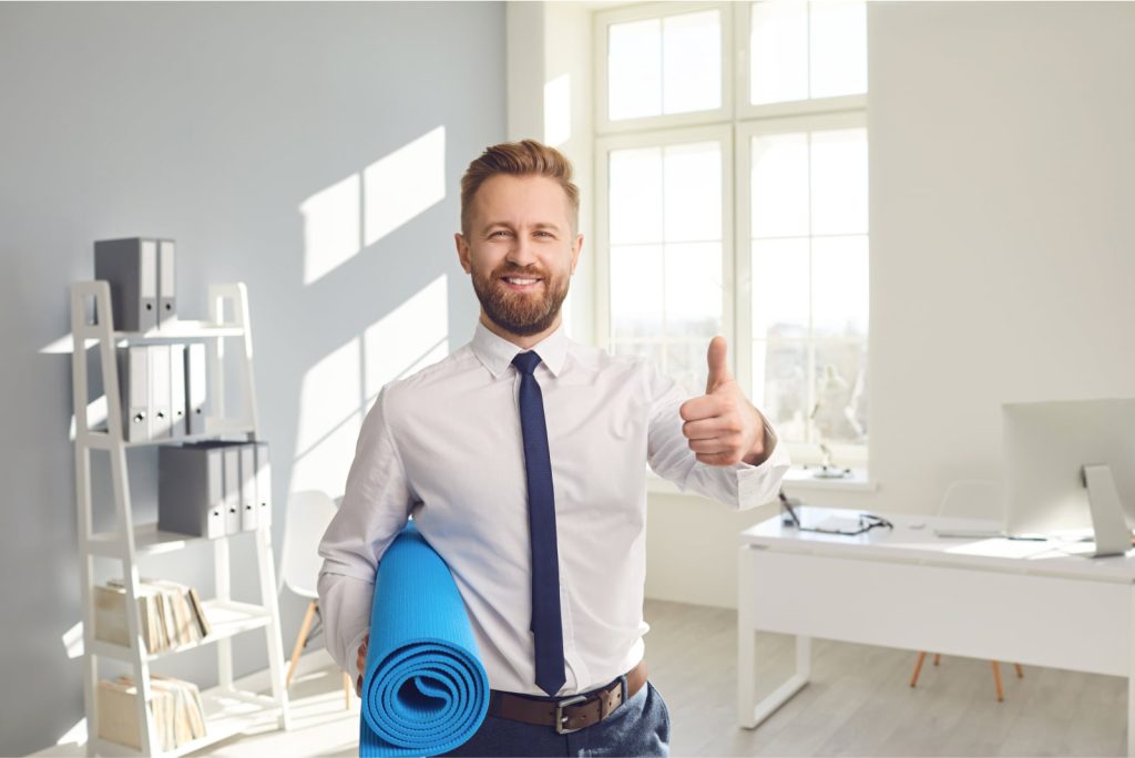 Happy businessman in a white shirt standing in an office, holding a yoga mat