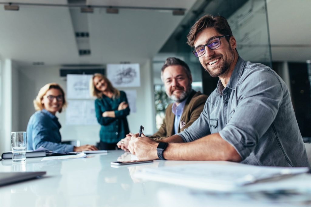 Four people, including a young designer holding a pen, smiling and looking at the camera in a conference room.