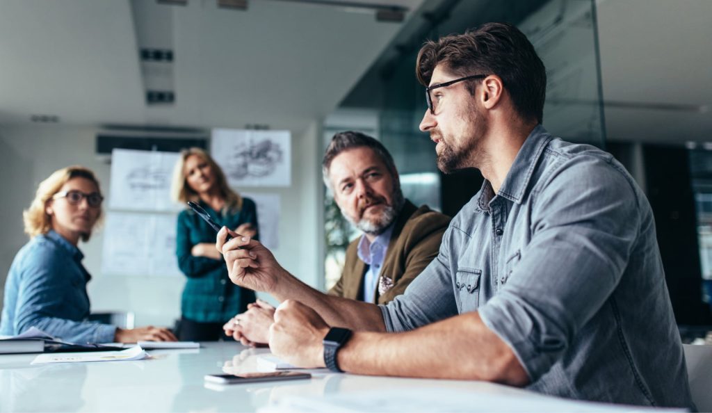 Young designer holding a pen and sharing project ideas with partners in a conference room, while the team listens attentively.