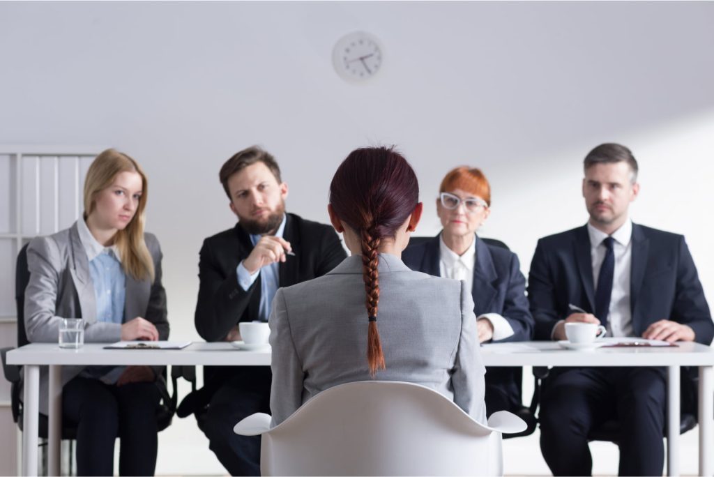 Woman with her back to the camera during a job interview, facing four members of the management team.