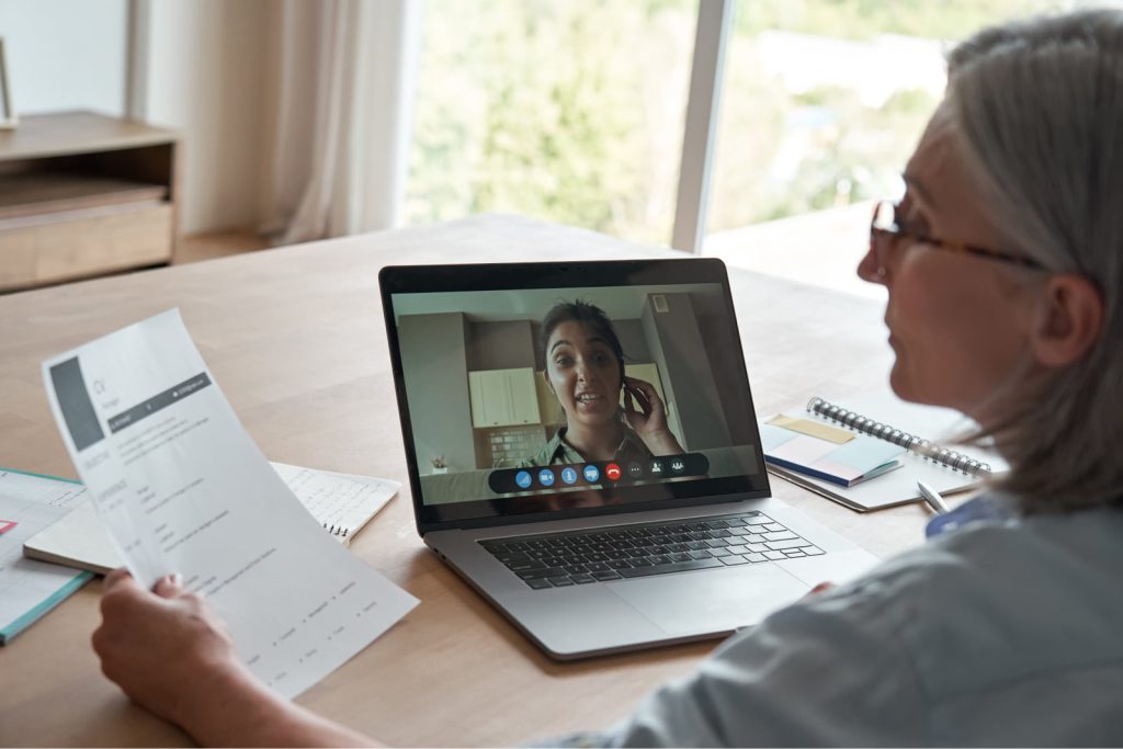 Older female HR professional reading a CV during an online job interview by video call.