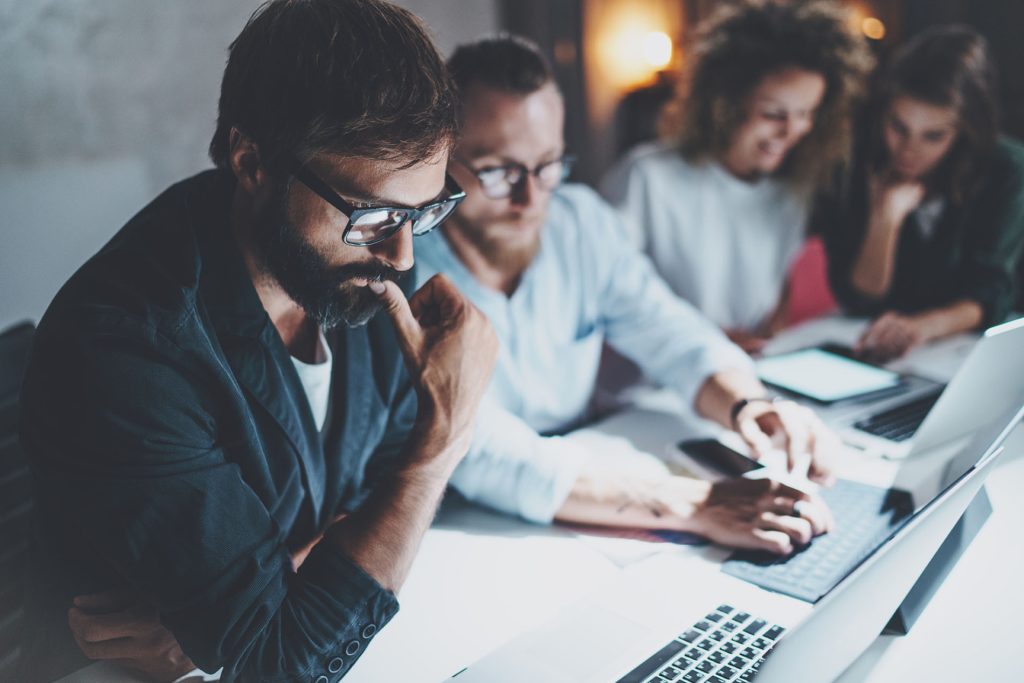 A group of focused professionals working together on laptops in a dimly lit office.