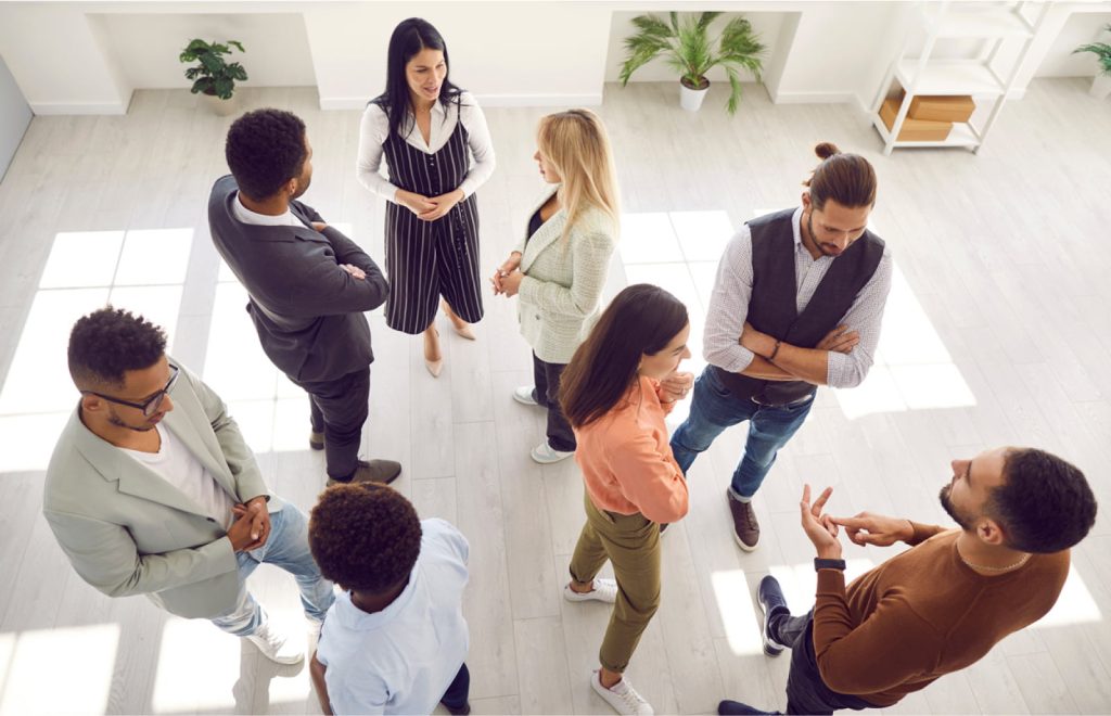 Groups of multi-ethnic people standing in an office, engaged in conversation during a casual corporate meeting.