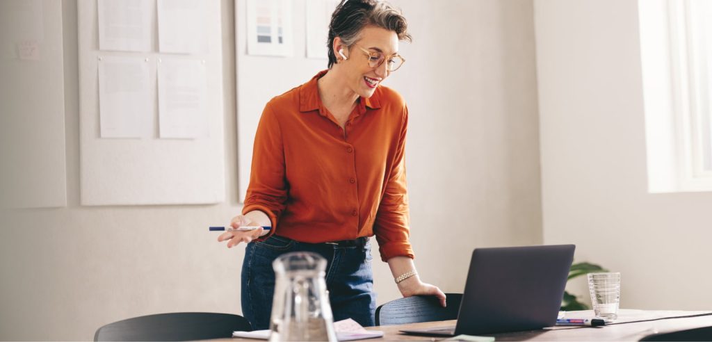 Mature businesswoman working remotely in a creative office, talking on the phone with earbuds in