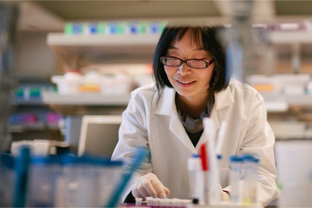 Female scientist in a biomedical laboratory wearing a lab coat and gloves.