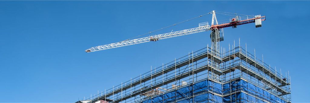 Construction crane working on a high-rise multistory building on a sunny day with a clear blue sky and no clouds.