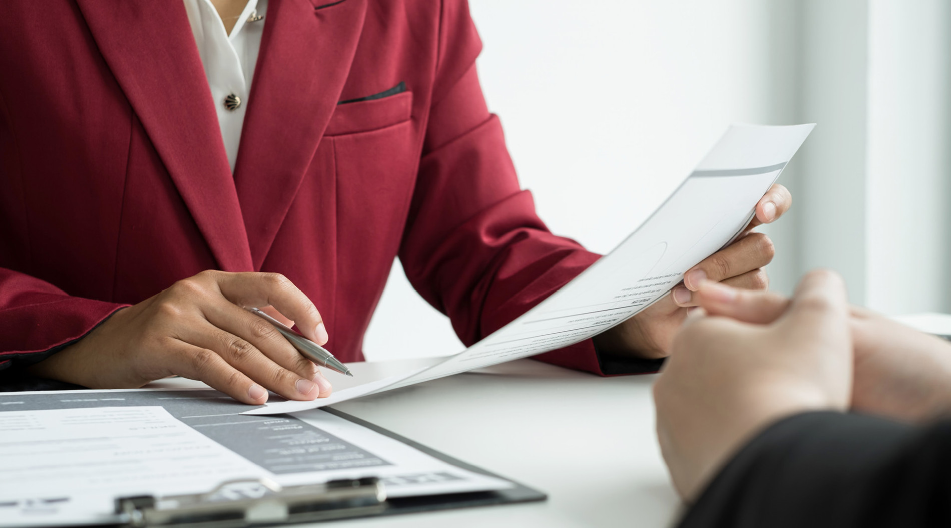 Person in a red blazer reviewing documents during a meeting.