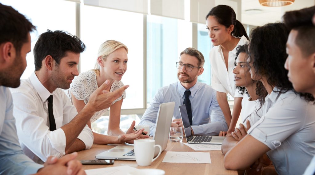 A group of business professionals is engaged in a serious discussion around a conference table in a modern office.