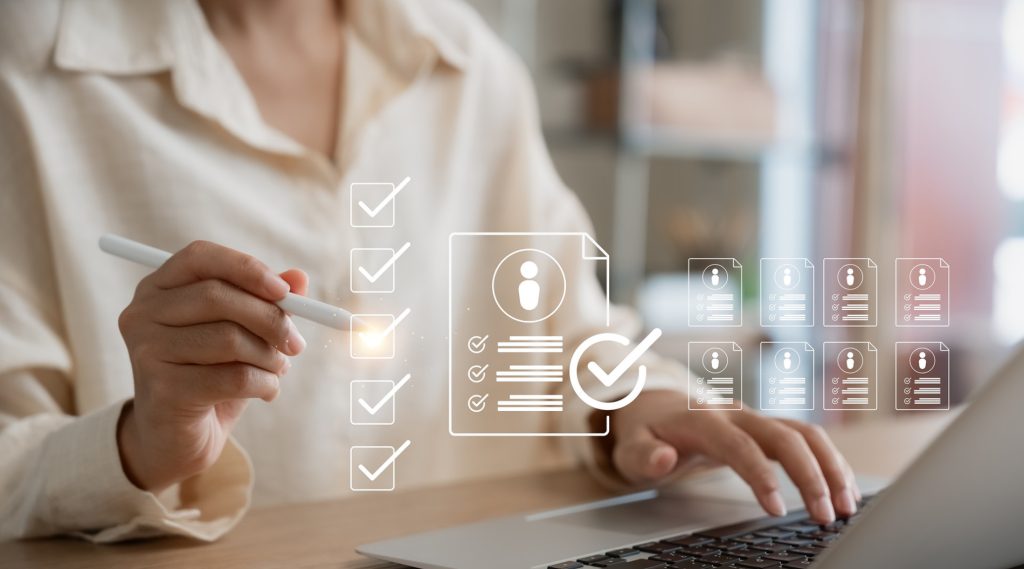 A person uses a stylus to check off items on a digital checklist displayed on a laptop screen, with icons representing documents and profiles.