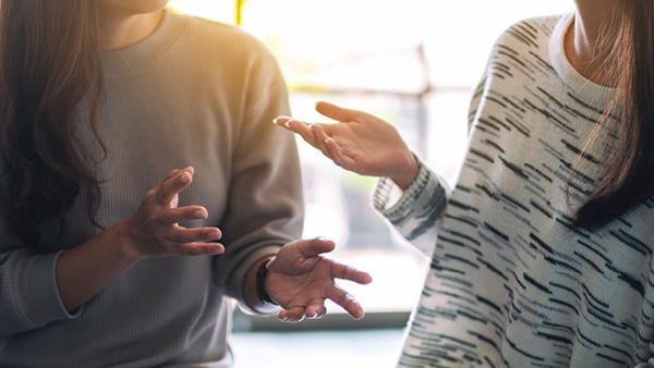 Two people engaged in a close, animated conversation, with hands gesturing expressively while discussing a topic.