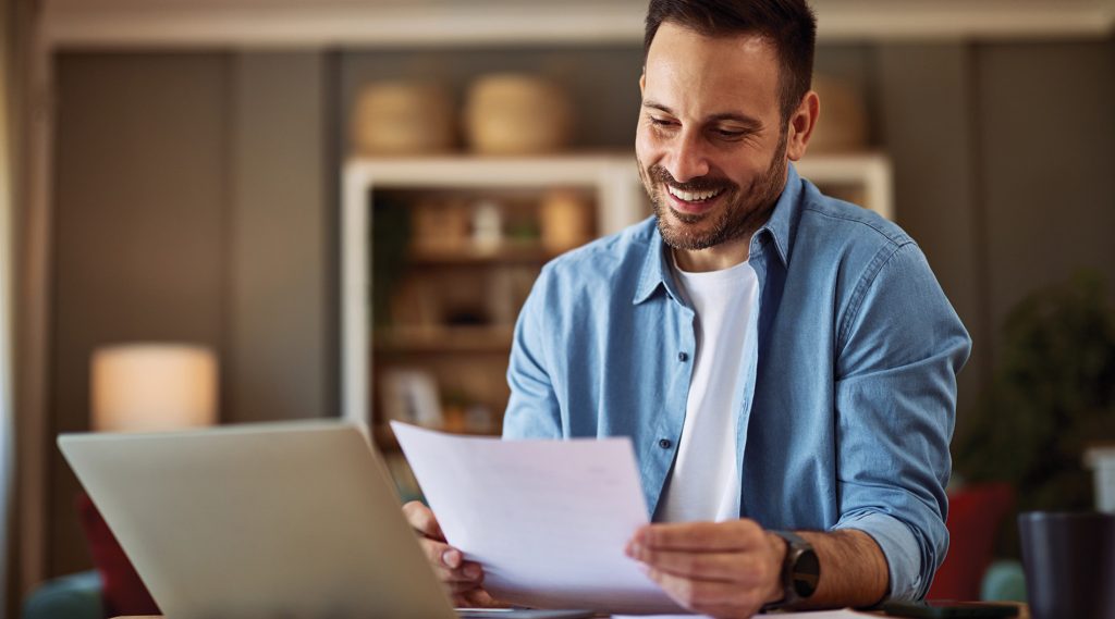 A happy and hopeful young adult man reading and checking his resume before applying for a new job.