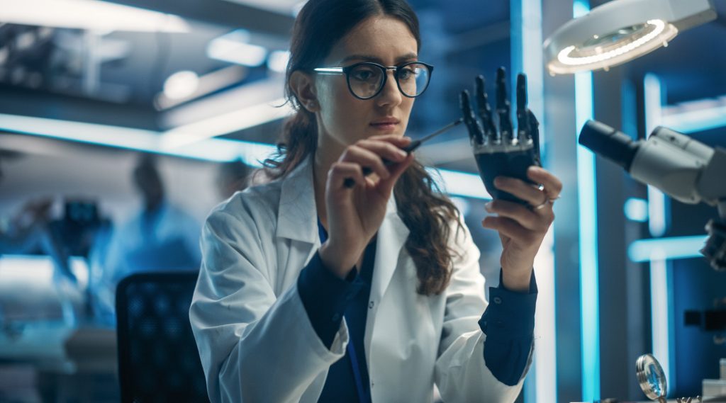 Female scientist examining a robotic hand in a high-tech laboratory.