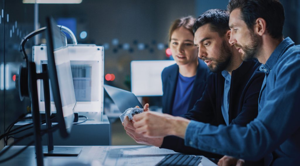 Team of engineers examining a 3D-printed object in a modern tech lab.