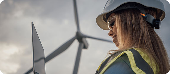 An engineer working on a laptop near a wind turbine, showcasing innovation in energy recruitment.