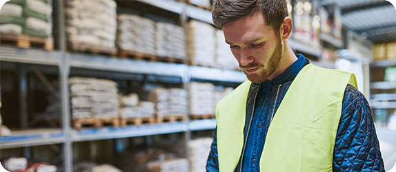 A warehouse employee checking inventory on a tablet in a well-organised storage area.