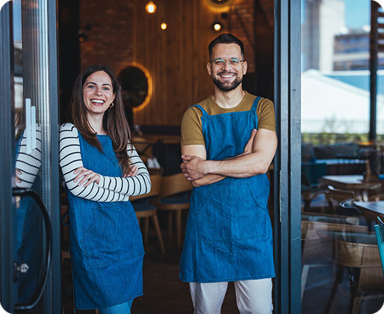 Smiling café owners standing proudly in front of their establishment, showcasing teamwork in hospitality.