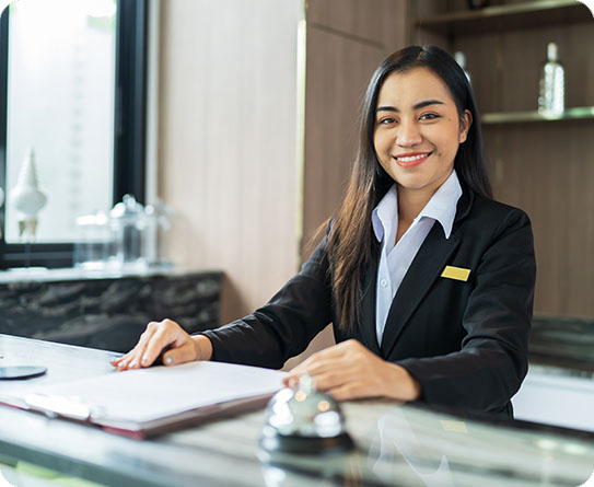 Smiling hotel receptionist at the front desk, ready to assist guests in a professional manner.