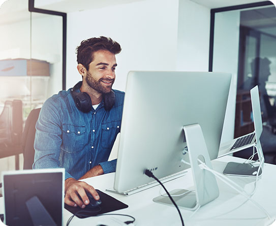 Smiling IT professional working at a desktop computer in a modern office setting, wearing headphones.