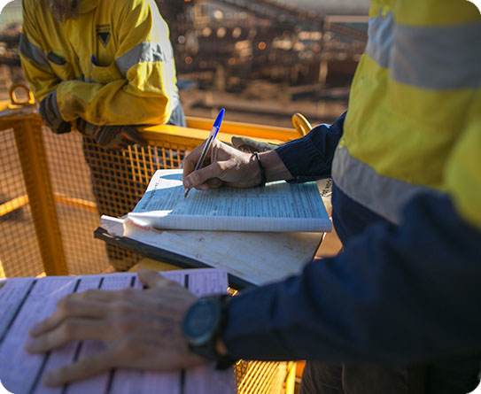 Close-up of mining professionals reviewing documentation on-site, highlighting teamwork and precision in the mining industry.