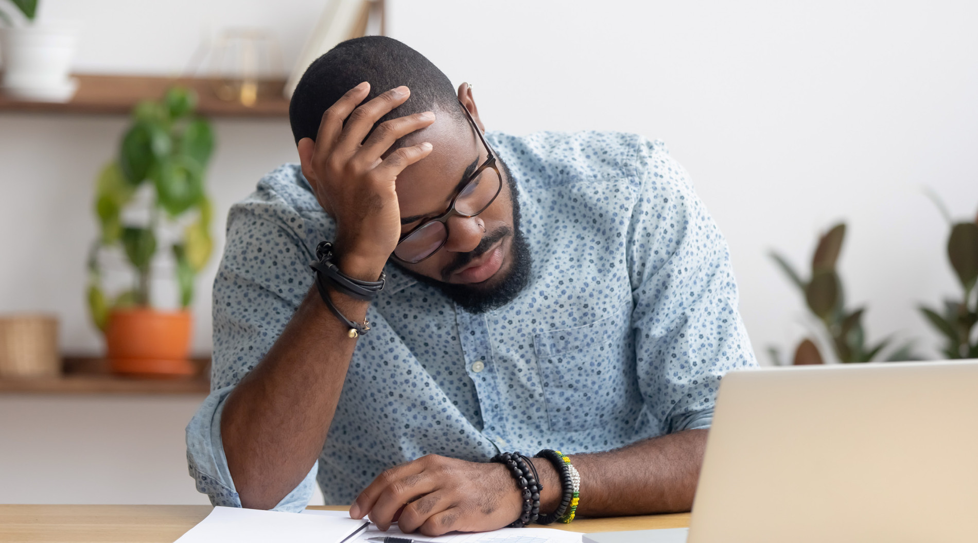 A man looking sad after losing his job, looking at his laptop with his CV in front of him