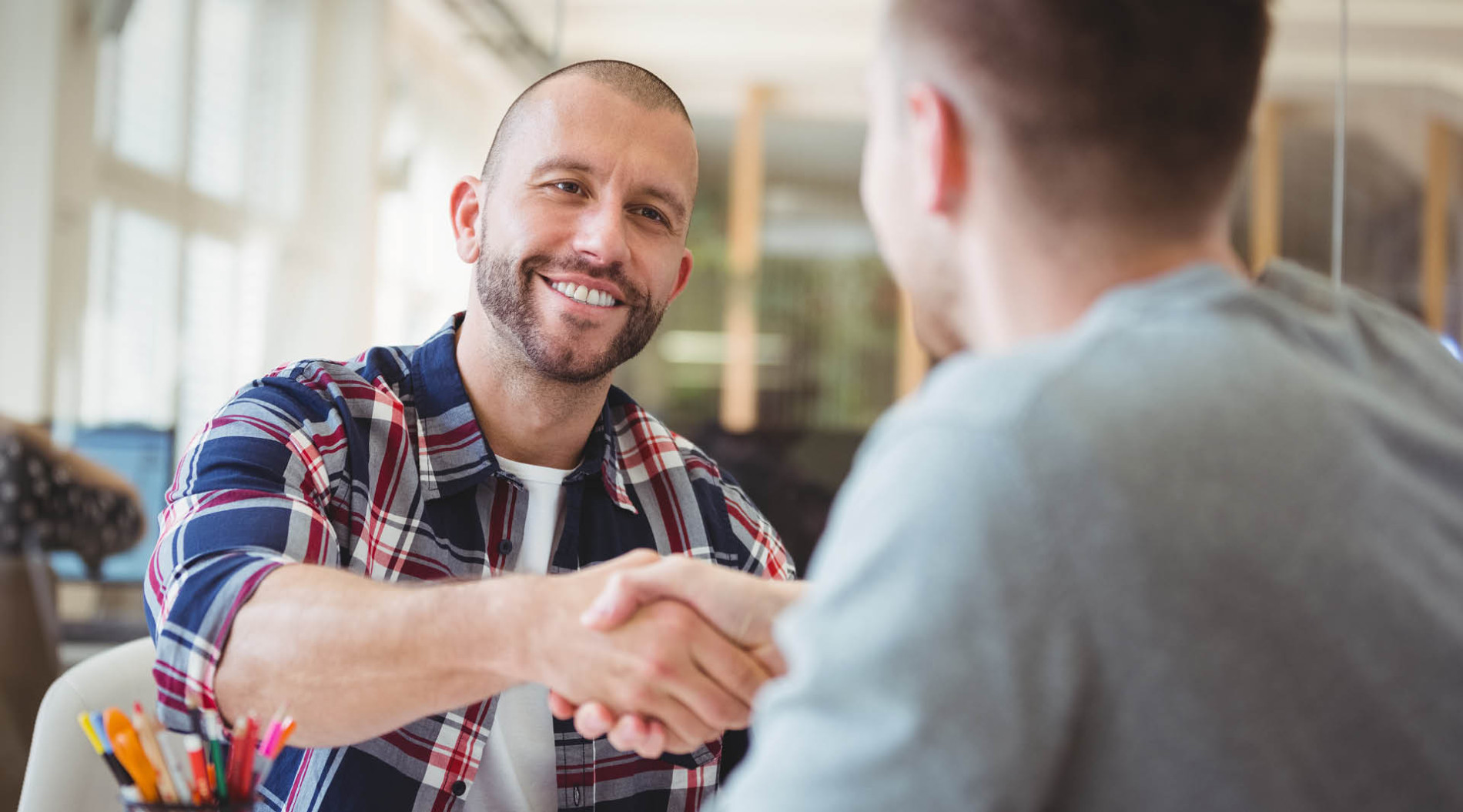 Two people shaking hands during a job interview. Both people are smiling.