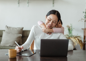 Women working at at desk with child hugging her from behind 