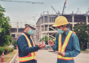 Workers in high vis jackets with hats and face masks on outside a construction site 