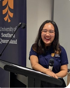 Nathalie, Q-ACE student standing at a lectern smiling