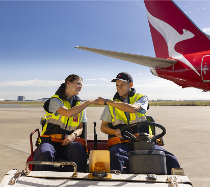 Two Qantas engineering employees driving on the tarmac with a Qantas plane in the background