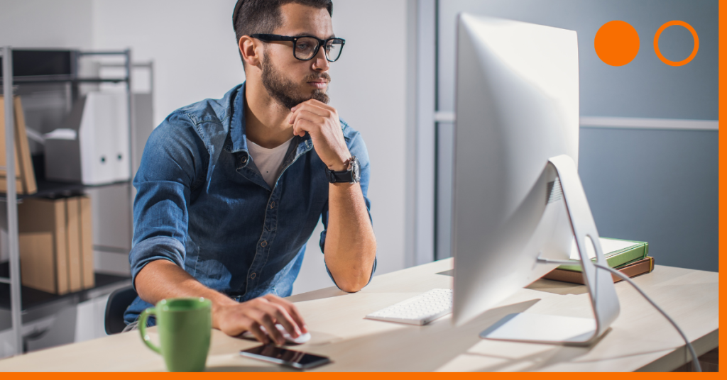 Man with elbow on desk, holding his chin and using desktop computer.