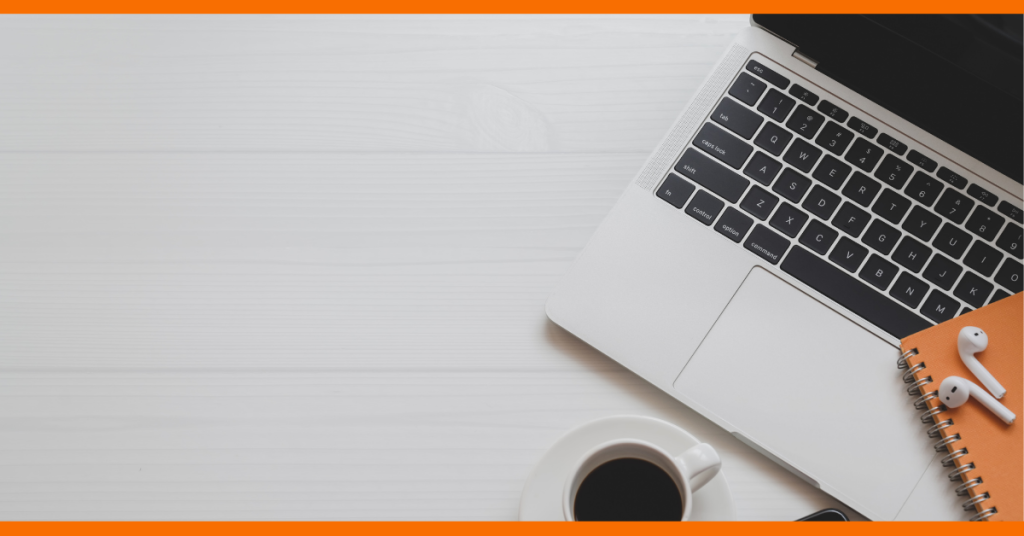 Laptop on the right hand side partially cut off with notebook and earpods sitting on top of the keyboard and mug of coffee in front of it on desk.