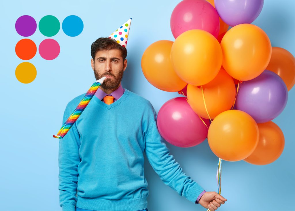 Man looking unmotivated wearing a party hat, party blower and holding balloons