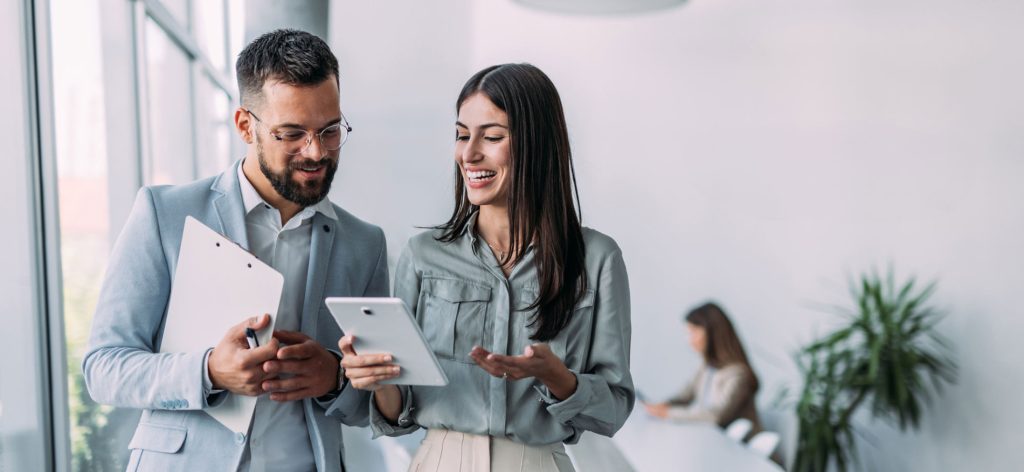 Two professionals discussing work while reviewing information on a tablet in a modern office setting.
