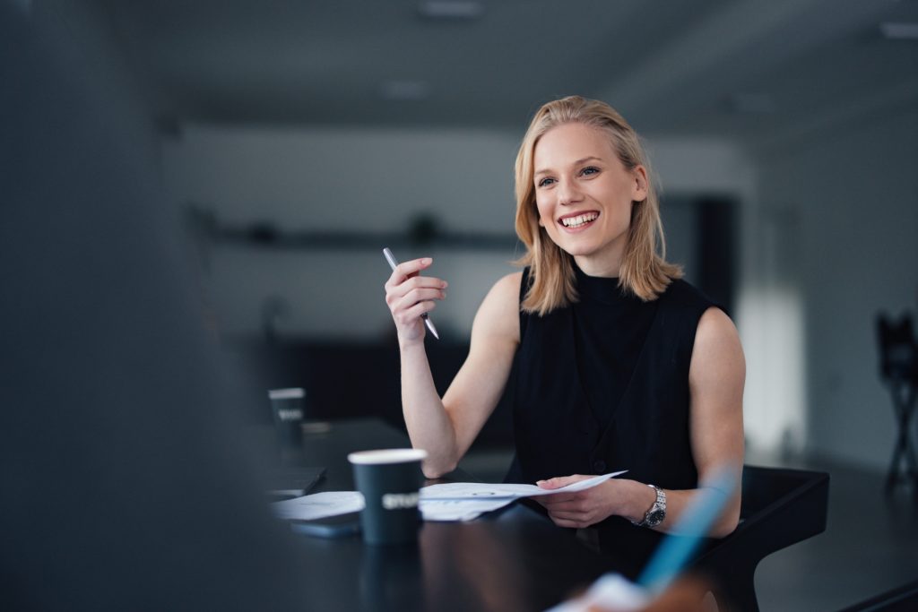 Contracts Administrator reviewing paperwork and discussing project details in a meeting, seated in a modern office environment.