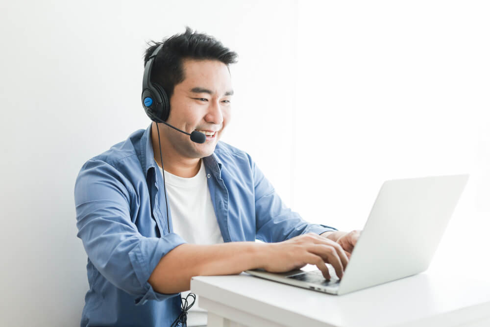 asian handsome man blue shirt using laptop with headphone talking smile happy face