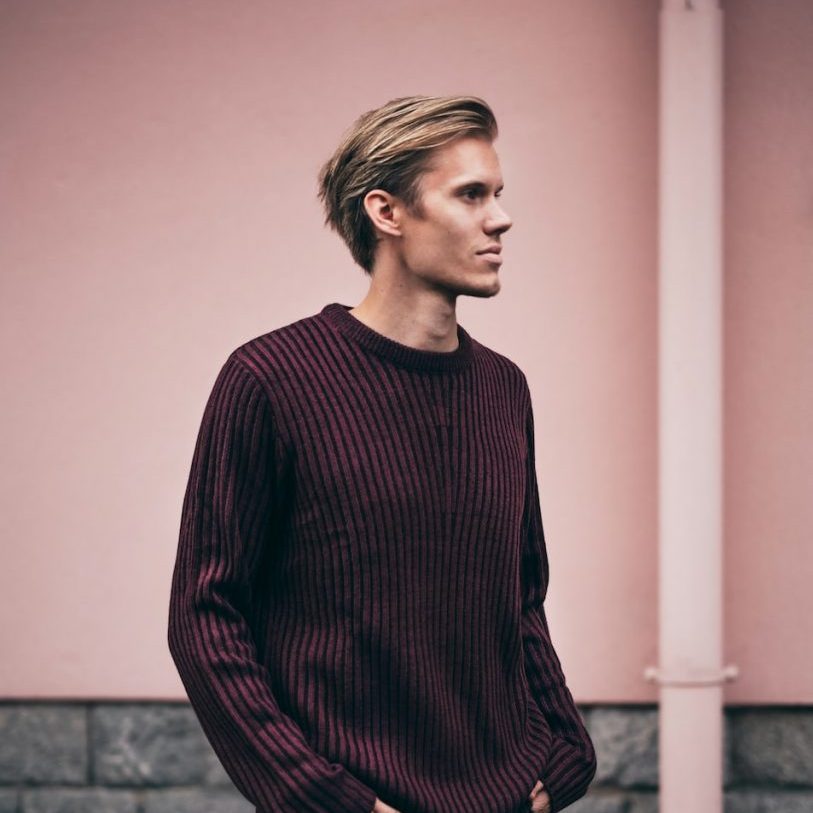 man in brown sweater standing beside wall