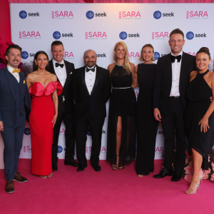 Eight people in total three men and four women taking a group photo in celebration of winning an award.