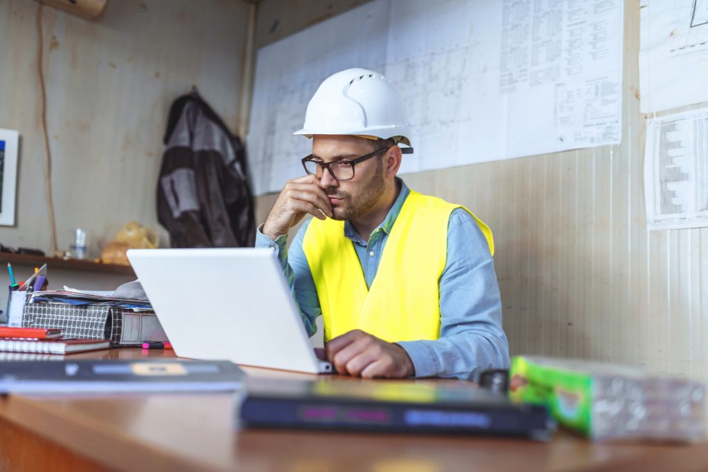 Business manager using laptop to review trade and engineering CVs and book candidate interviews online.