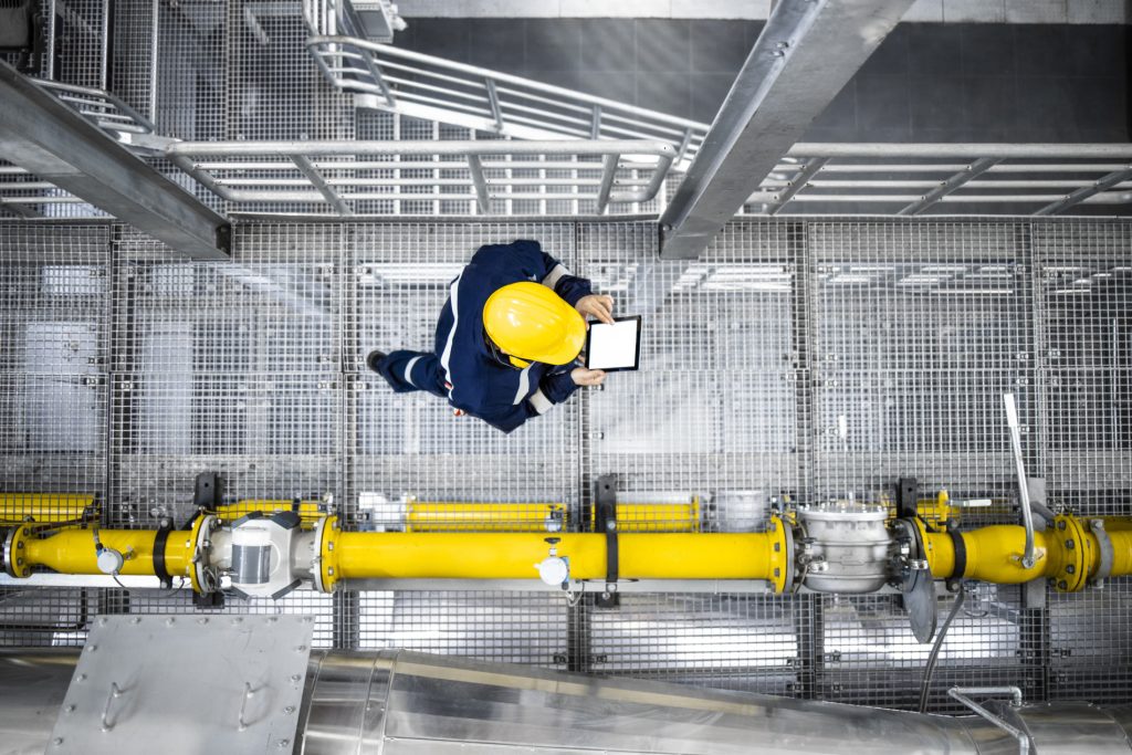 Tradesperson in PPE working on industrial pipe system, representing new oil and gas job opportunities.