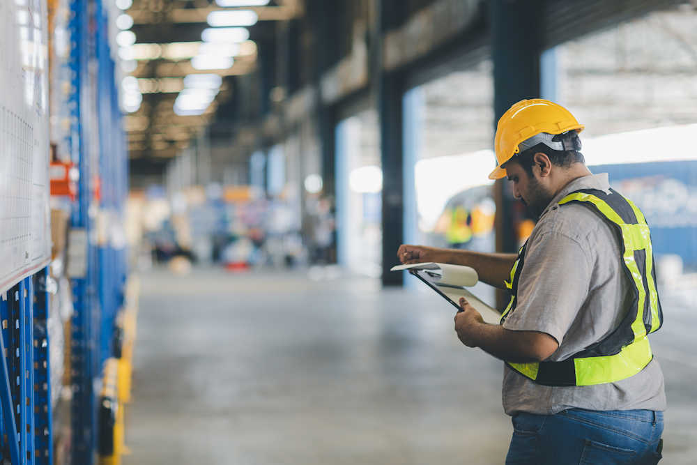 TechTrade warehouse operations worker reviewing inventory in industrial storage facility